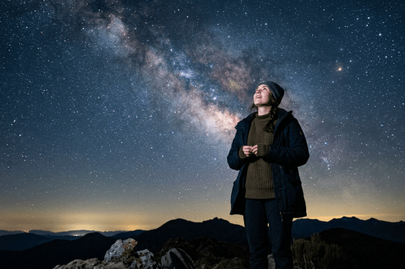 Person standing outdoors at night looking up at the Milky Way galaxy in the star-filled sky
